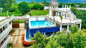 A hotel with a swimming pool, a tower, and a view of mountains.