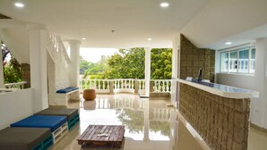 A spacious room with a balcony, a reception desk, and a seating area with cushions.