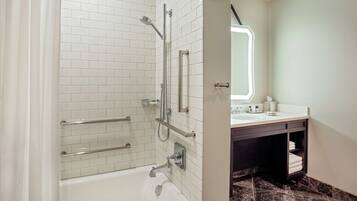 Un baño moderno con azulejos blancos tipo metro, una bañera blanca, ducha con mampara de vidrio y un mueble de tocador oscuro con espejo.