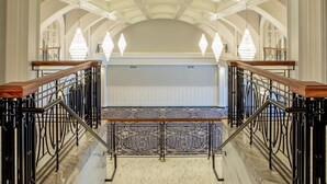 Una imponente escalera con barandales negros ornamentales y piso de mármol, que conduce a un techo alto con tragaluz.