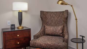 A bedroom with a wooden nightstand, a lamp, a chair, and a small round table.