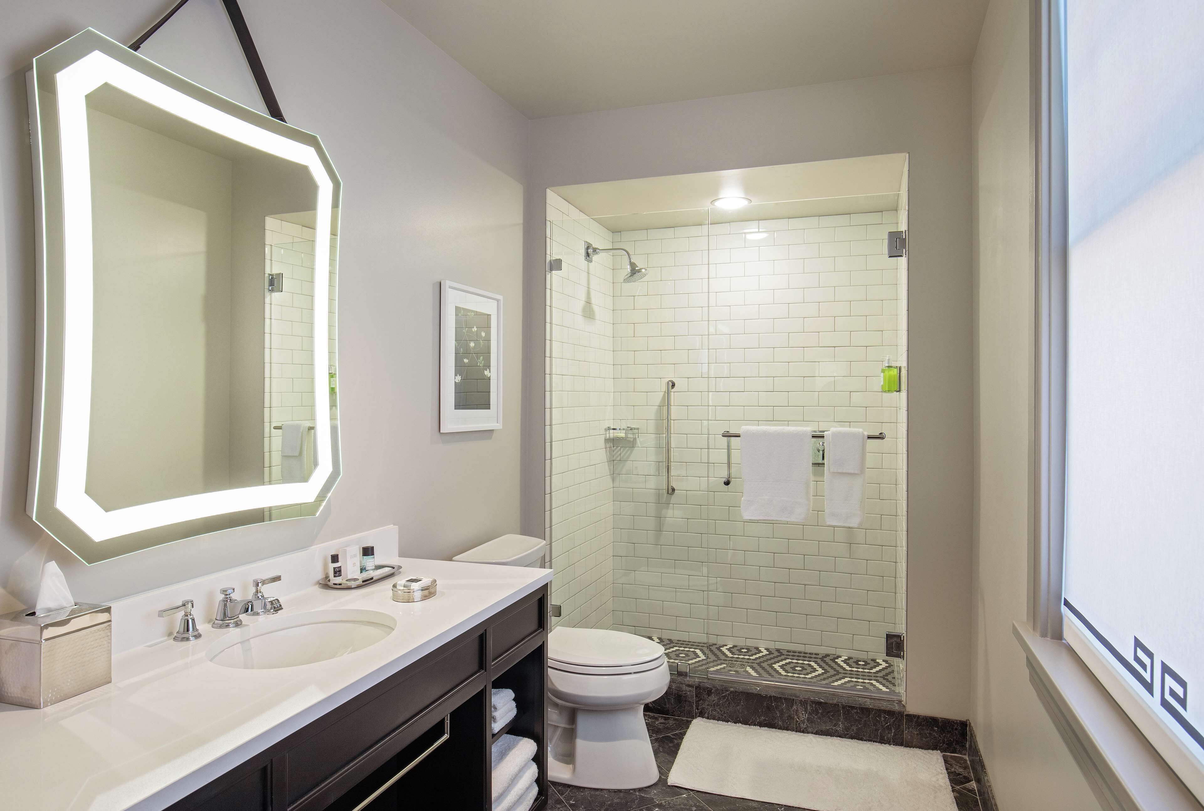 Een moderne badkamer met een grote spiegel, dubbele wasbakken, toilet en een douchehoek.