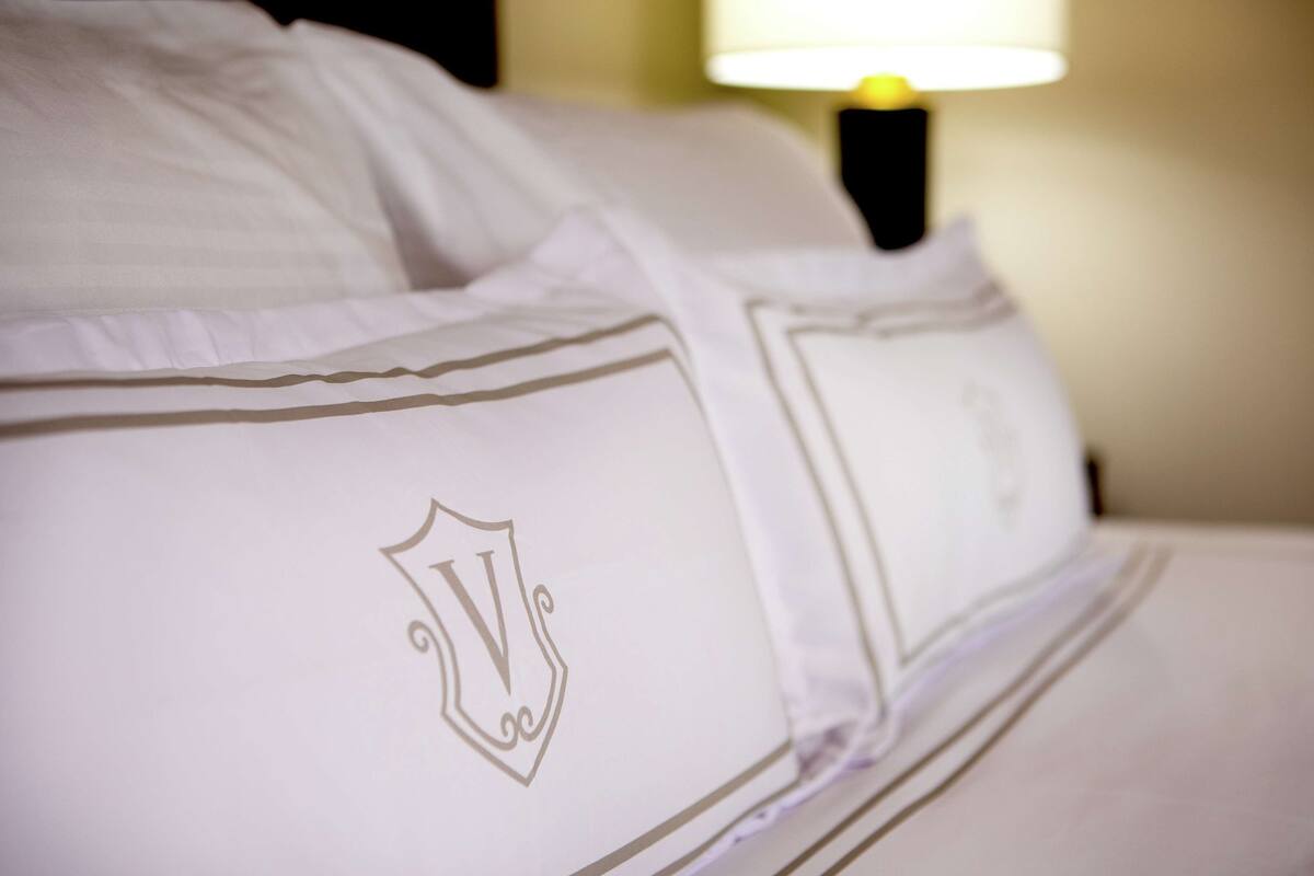 Een net opgemaakt bed met witte lakens en een decoratief symbool op het kussen.