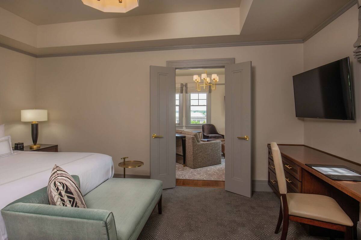 Een hotelkamer met een bed, een bureau, een televisie, een stoel en uitzicht door een geopende deur.