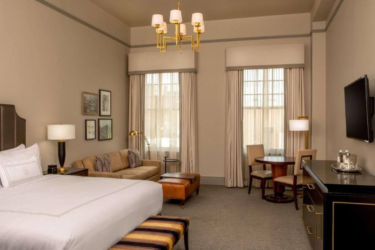 Een hotelkamer met een groot bed, een bank, een bureau met stoel, een televisie en een kroonluchter.