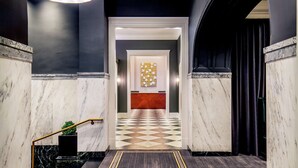 Un vestíbulo de hotel con piso a cuadros, paredes de mármol, un mostrador de recepción y una araña.
