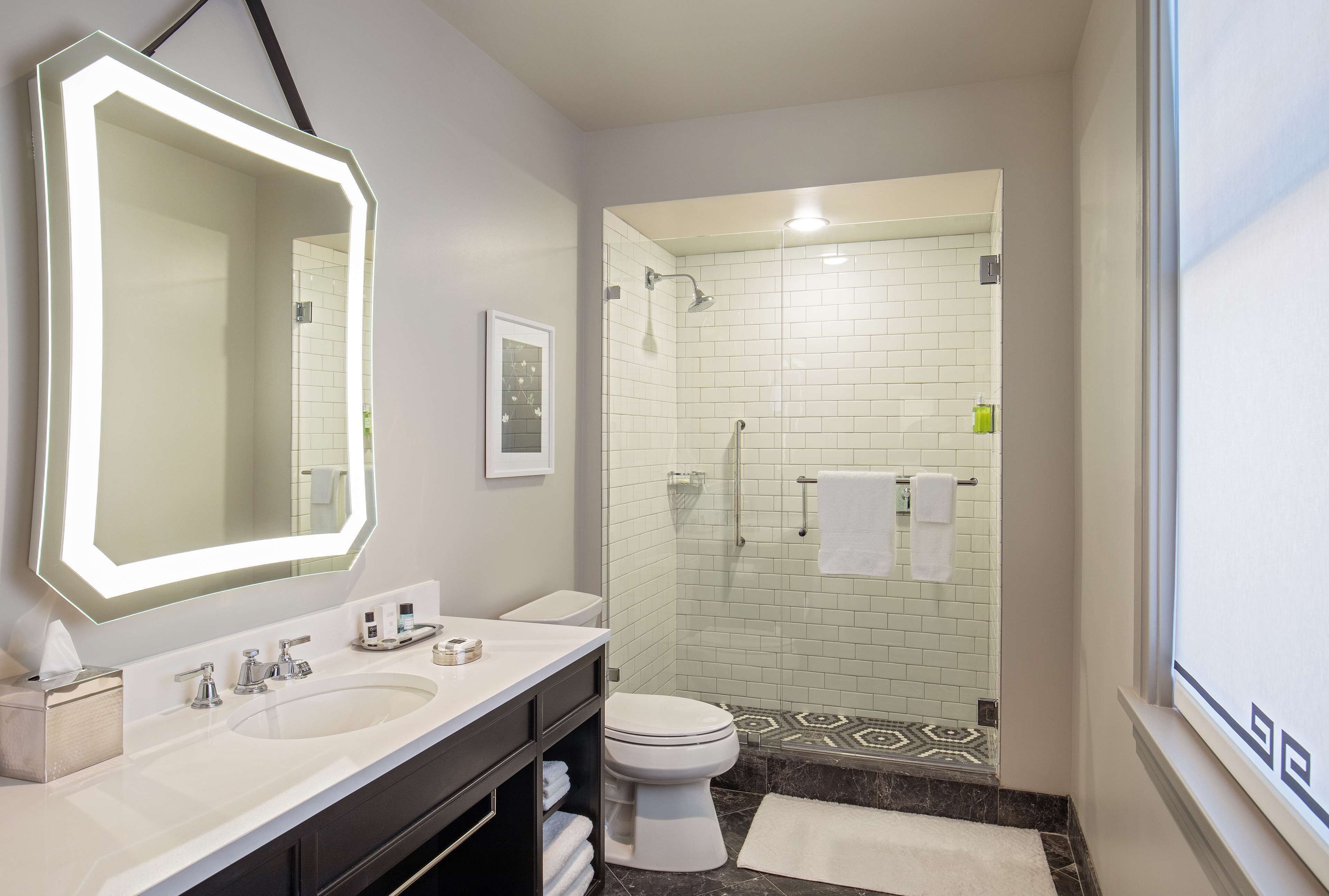 A modern bathroom with a large mirror, dual sinks, a toilet, and a shower area.
