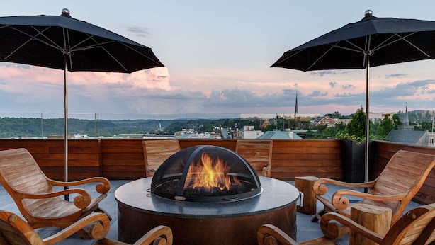 Una terraza en la azotea con un pozo de fuego circular rodeado de sillas de madera y dos sombrillas.