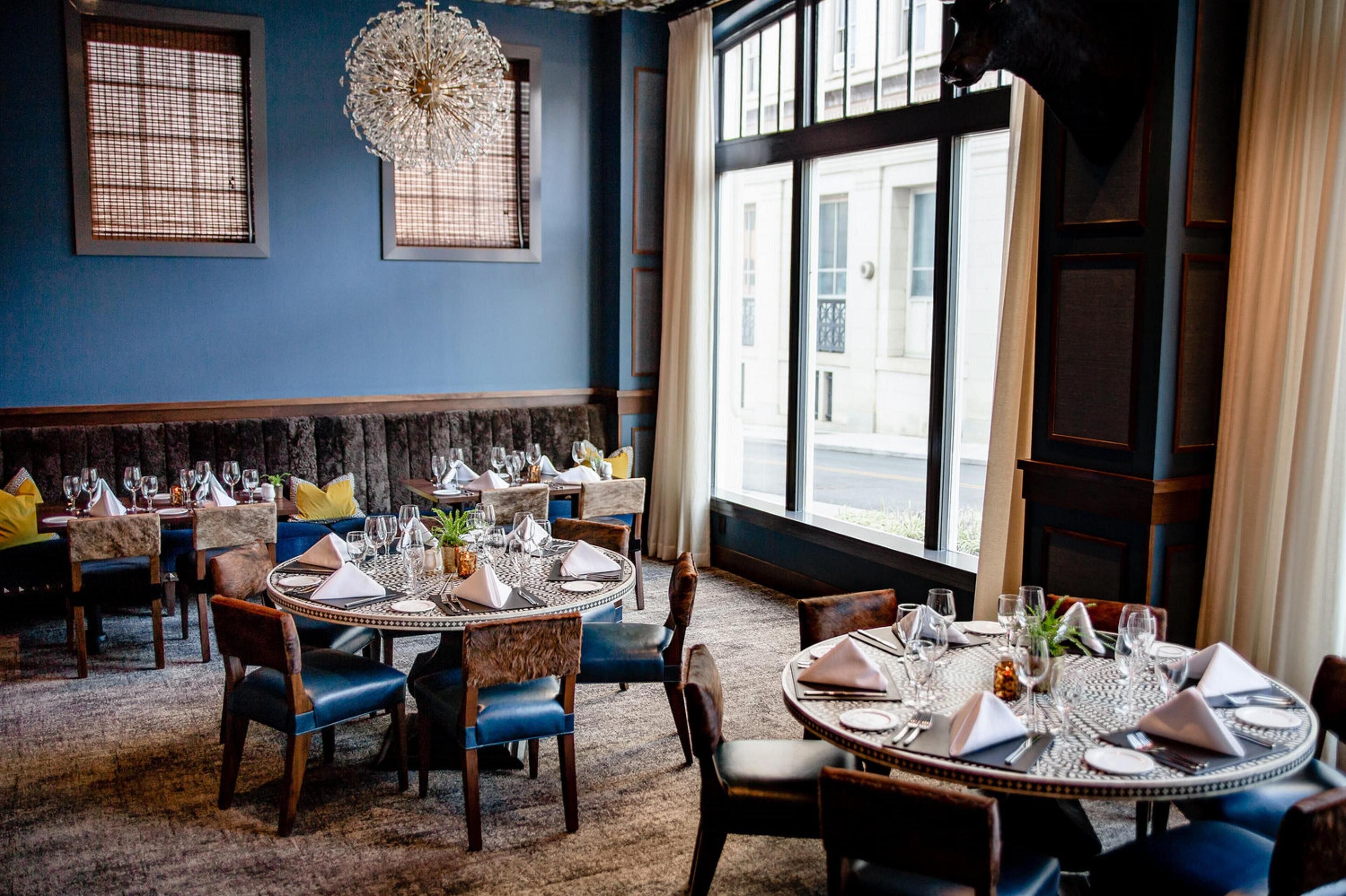 A dining area with round tables set for four, featuring a central floral arrangement.