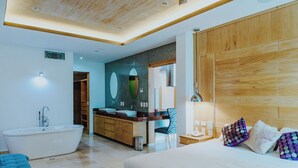 Quarto de hotel moderno com uma cama grande, banheiro separado com banheira, toucador com espelho e cabeceira de madeira.