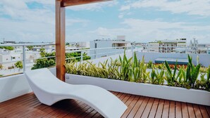 Terraço no telhado com uma cadeira de estar branca, deck de madeira e vista para a cidade e oceano.
