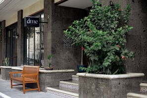 L’entrée d’un hôtel, avec un banc en bois, des plantes en pot et une enseigne indiquant « Ame Hotel & Spa ».
