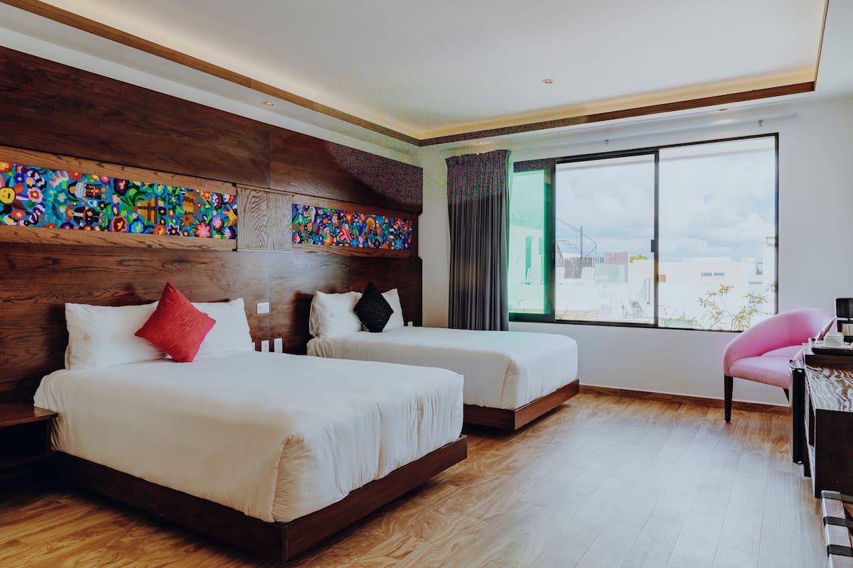 Ein Hotelzimmer mit zwei Betten, einem hölzernen Kopfteil, einem großen Fenster mit Blick und einem Schreibtisch mit Stuhl.