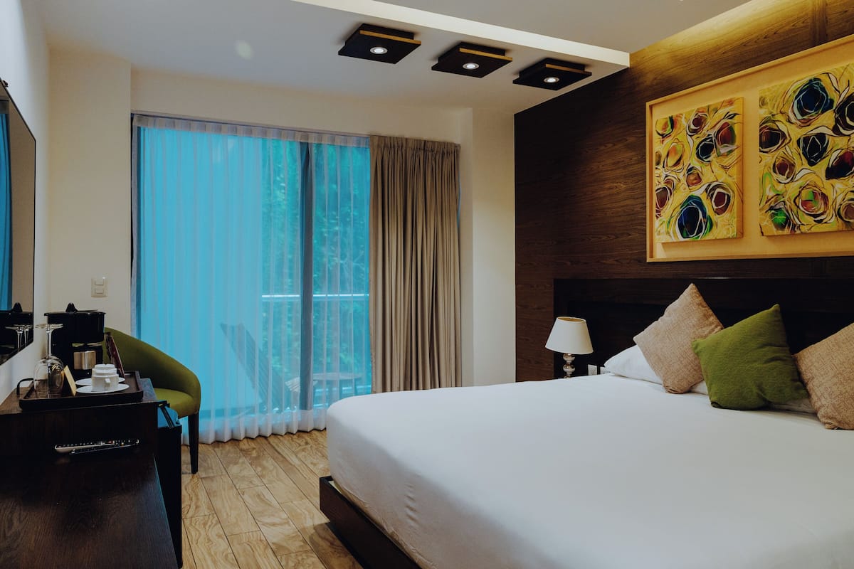 Ein Hotelzimmer mit einem großen Bett, einem Schreibtisch mit Lampe und Blick ins Freie durch das Fenster.