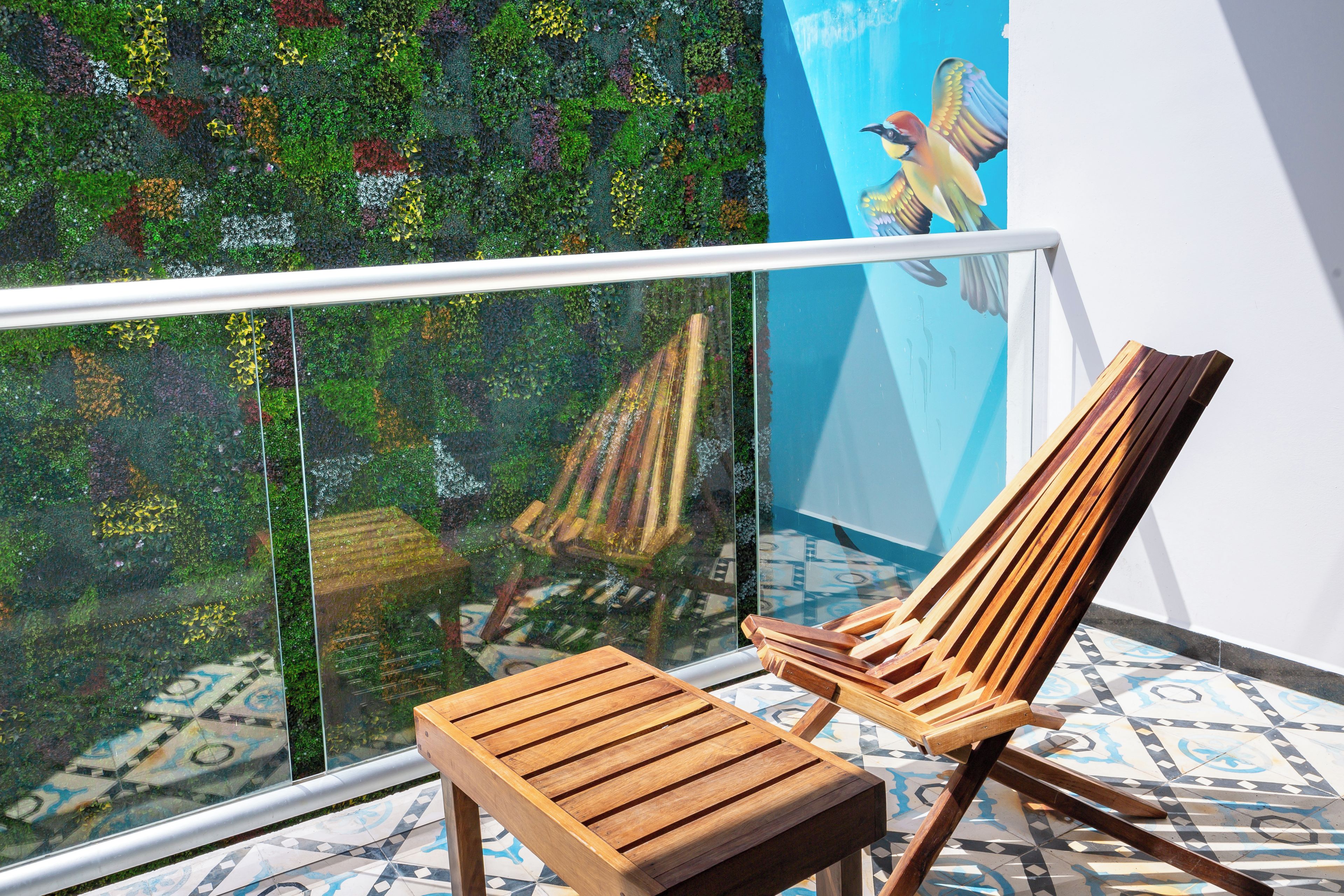 A wooden chair and a glass balustrade overlooking a patterned floor and a wall with a mural.