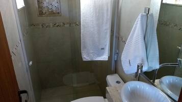 Un baño con ducha envuelta en vidrio, inodoro blanco y un lavamanos grande.