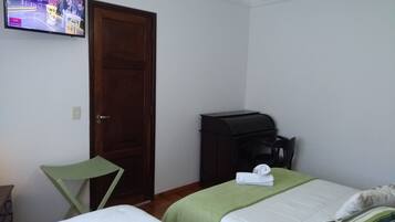 Quarto de hotel com duas camas, uma televisão na parede, uma porta de madeira e uma pequena mesa com uma chaleira.