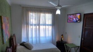 Habitación de hotel con dos camas, ventilador de techo, televisión y una puerta.