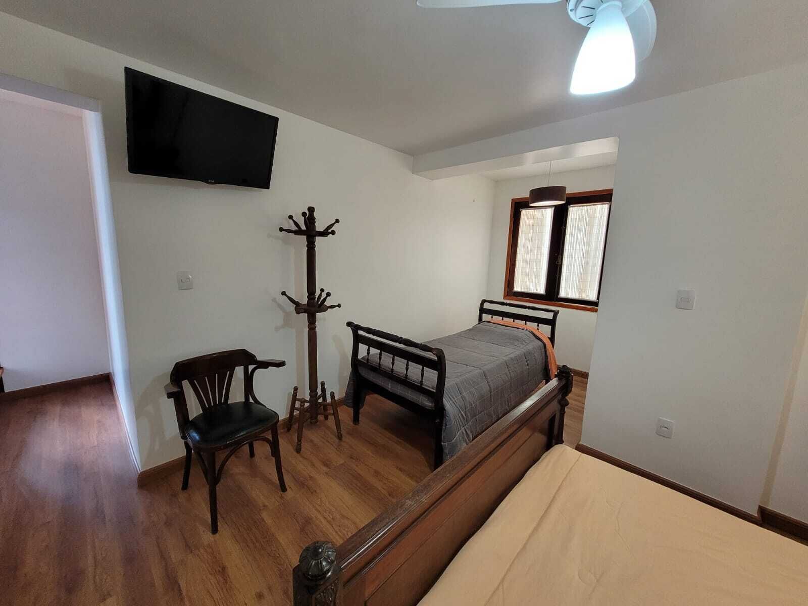 Un dormitorio con una cama, una silla, perchero, televisor y ventana.
