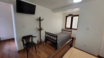 Un dormitorio con una cama, una silla, perchero, televisor y ventana.
