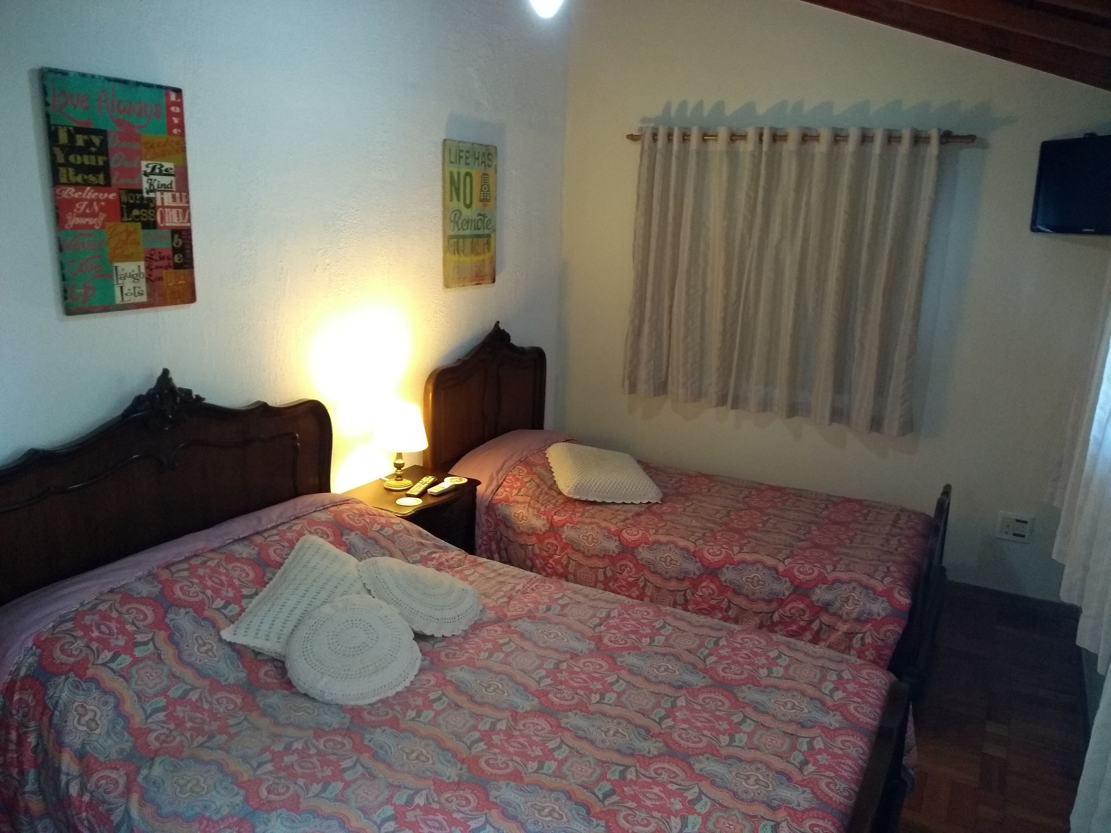 A room with two beds, each with a patterned bedspread and a white pillow. There is a nightstand with a lamp and a remote control. A sign on the wall reads "LIFE HAS NO LIMITS."