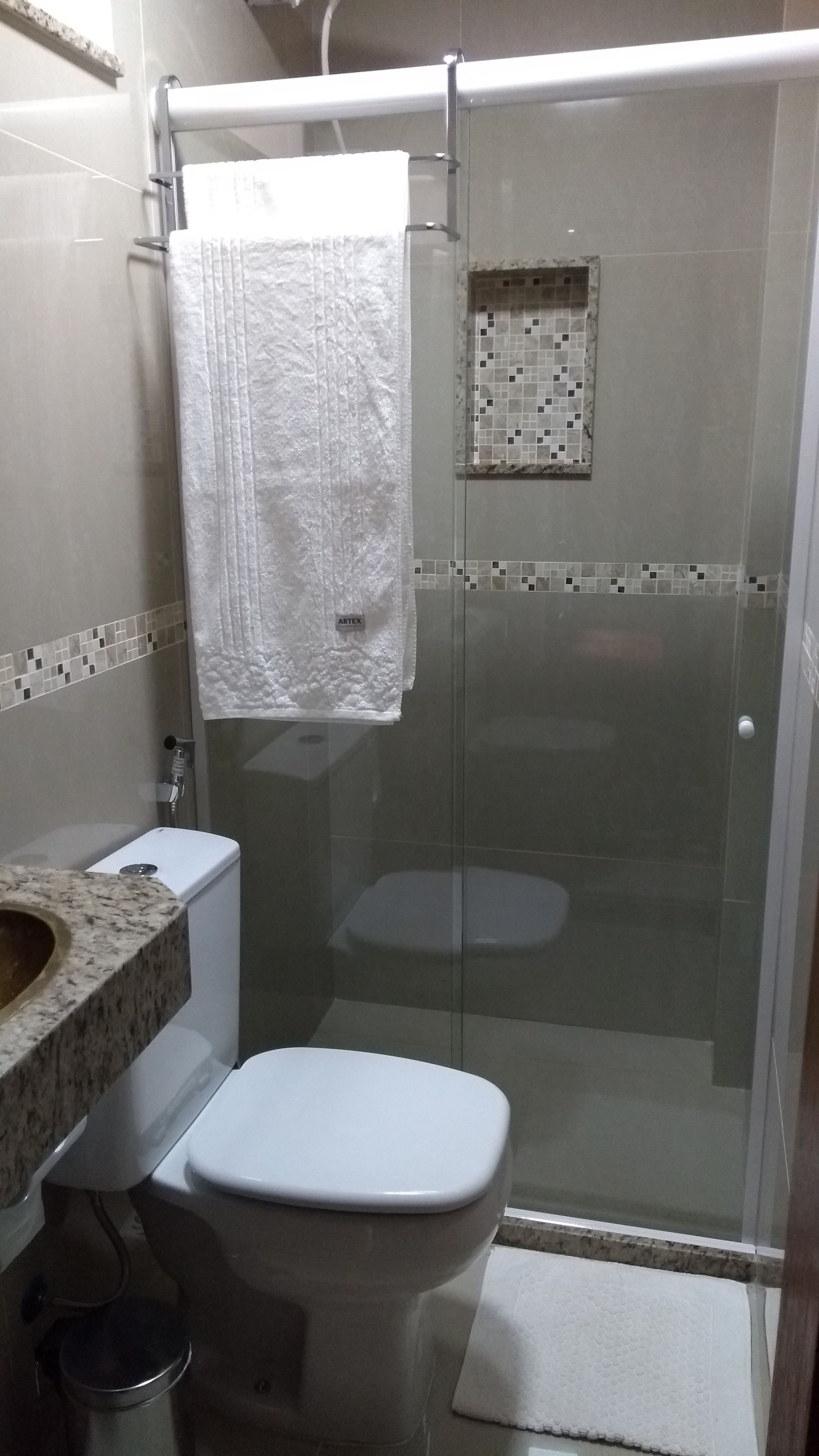 Un baño con ducha de vidrio, inodoro blanco y lavamanos de mármol.