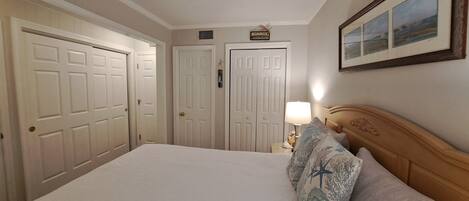 A hotel room with a bed, a nightstand with a lamp, a framed picture on the wall, and two doors.