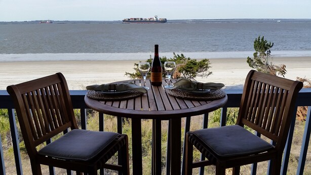 Une table en bois avec deux chaises, sur un balcon donnant sur une plage.