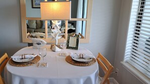 Une table à manger dressée avec une nappe blanche, des sets de table en tissu et des couverts en argent, et un miroir au-dessus qui reflète la pièce.