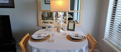 Mesa de comedor con mantel blanco, individuales tejidos y cubiertos, con un espejo que refleja la habitación.