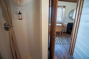 A doorway leading to a room with a wooden floor, a chair, a small table, and a mirror on the wall. - Codfish Cottage Cabin on the Strait of Juan de Fuca (Port Angeles)