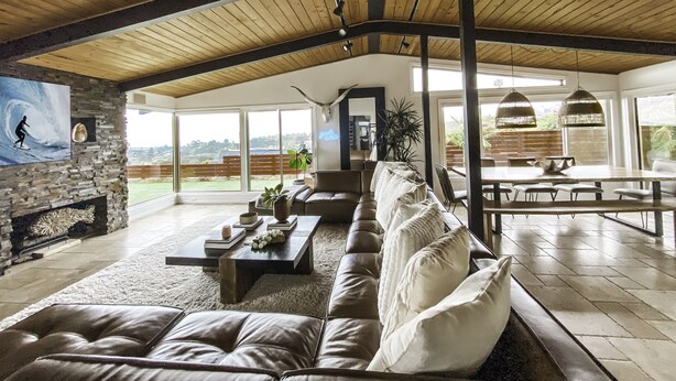 Een ruime woonkamer met hoge plafonds, een stenen muur en een groot raam met uitzicht op de omgeving.