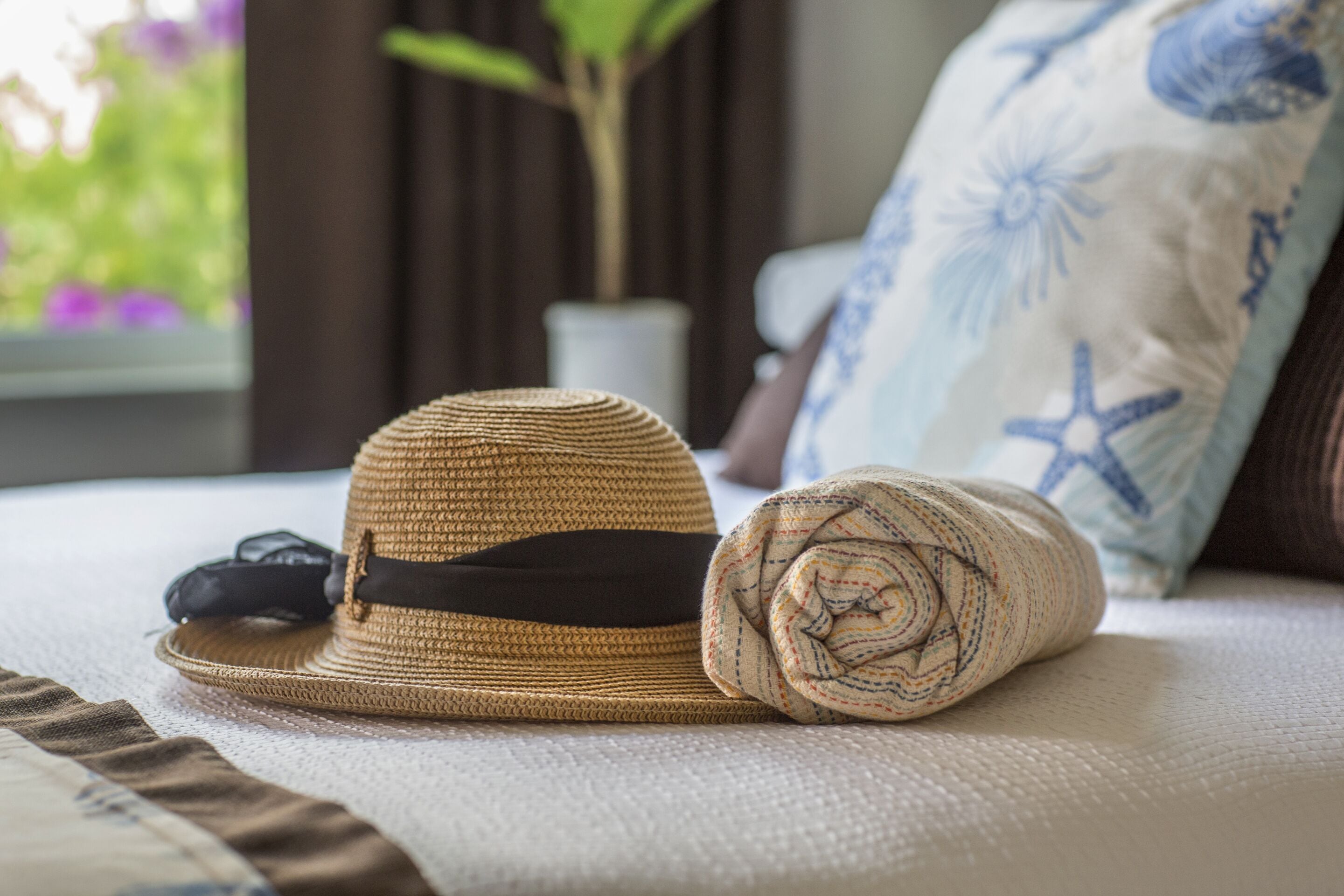 A bed with a straw hat and a rolled-up towel.