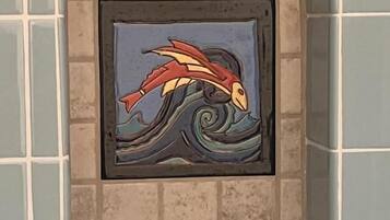 A framed artwork of a stylized fish in a wave pattern, set in a tiled alcove.