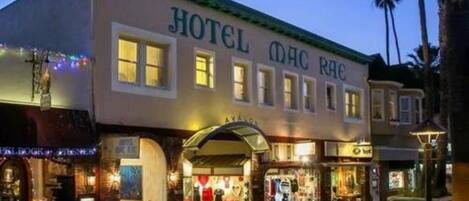 A hotel with a classic facade, multiple storefronts at the ground level, and a well-lit entrance.