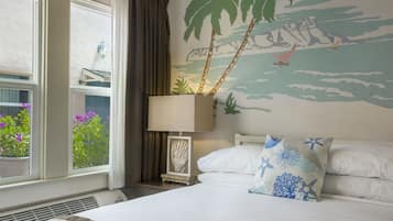 A hotel room with a bed, a nightstand with a lamp, a window with curtains, and a wall mural of a beach scene.