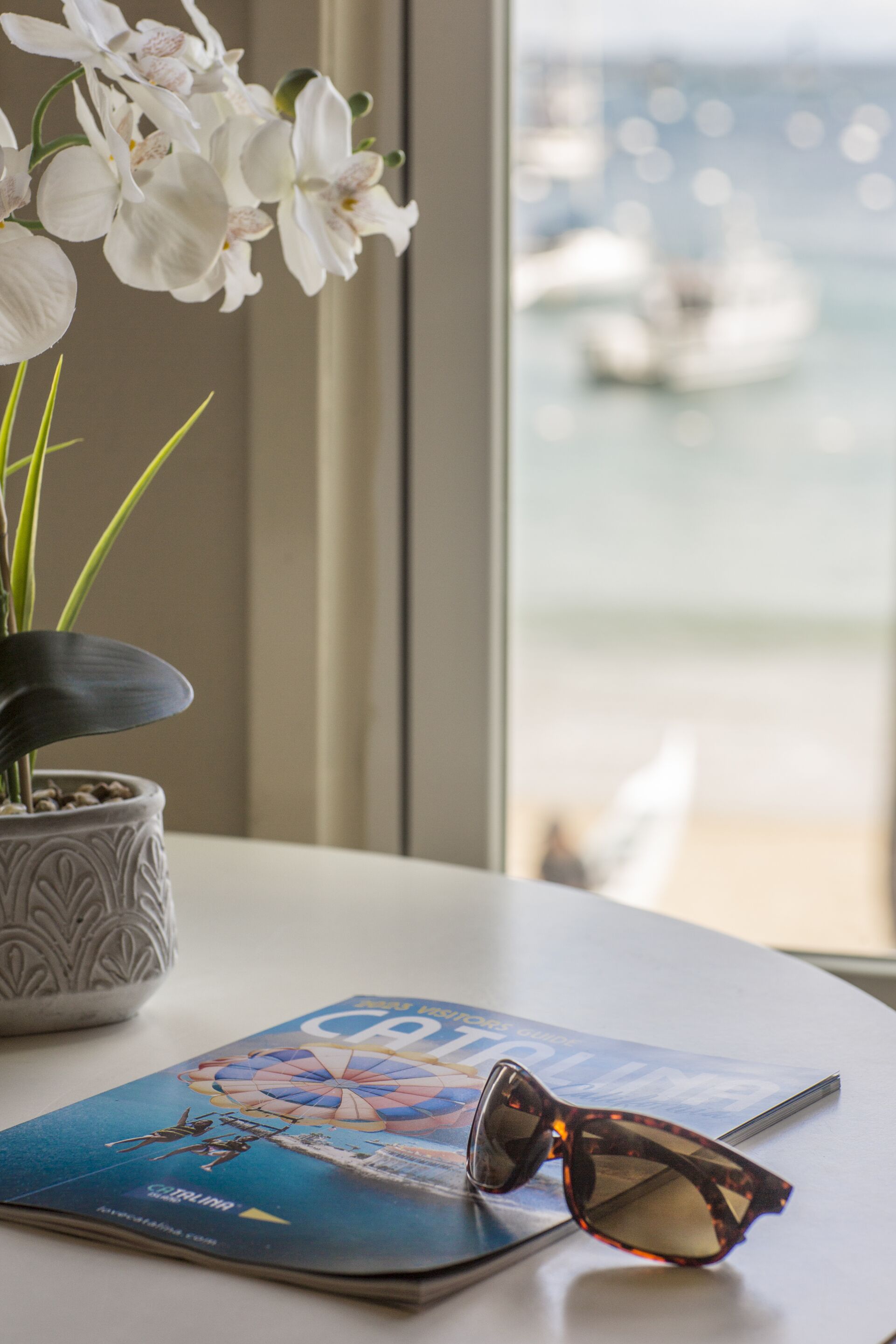 A table with a magazine, sunglasses, and a potted orchid.