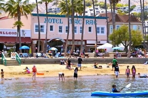 A hotel with a beach view, a swimming pool, and a beach area with people and a kayak.