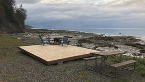 A wooden deck with a table and chairs overlooking a rocky shoreline and the ocean. - Ocean View Tent Site T12 (Port Angeles)