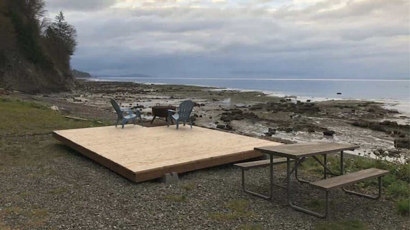 A wooden deck with a table and chairs overlooking a rocky shoreline and the ocean.