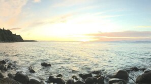 A coastal scene with a rocky shoreline and a calm sea under a sunset sky. - Ocean View Tent Site T12 (Port Angeles)