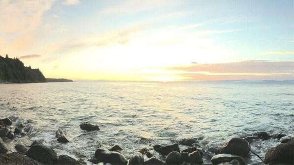 A coastal scene with a rocky shoreline and a calm sea under a sunset sky.