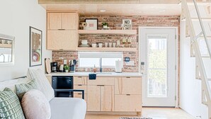 Una cucina moderna con mobili in legno, zoccolo in mattoni e zona pranzo con tavolo bianco e tappeto a motivi blu.