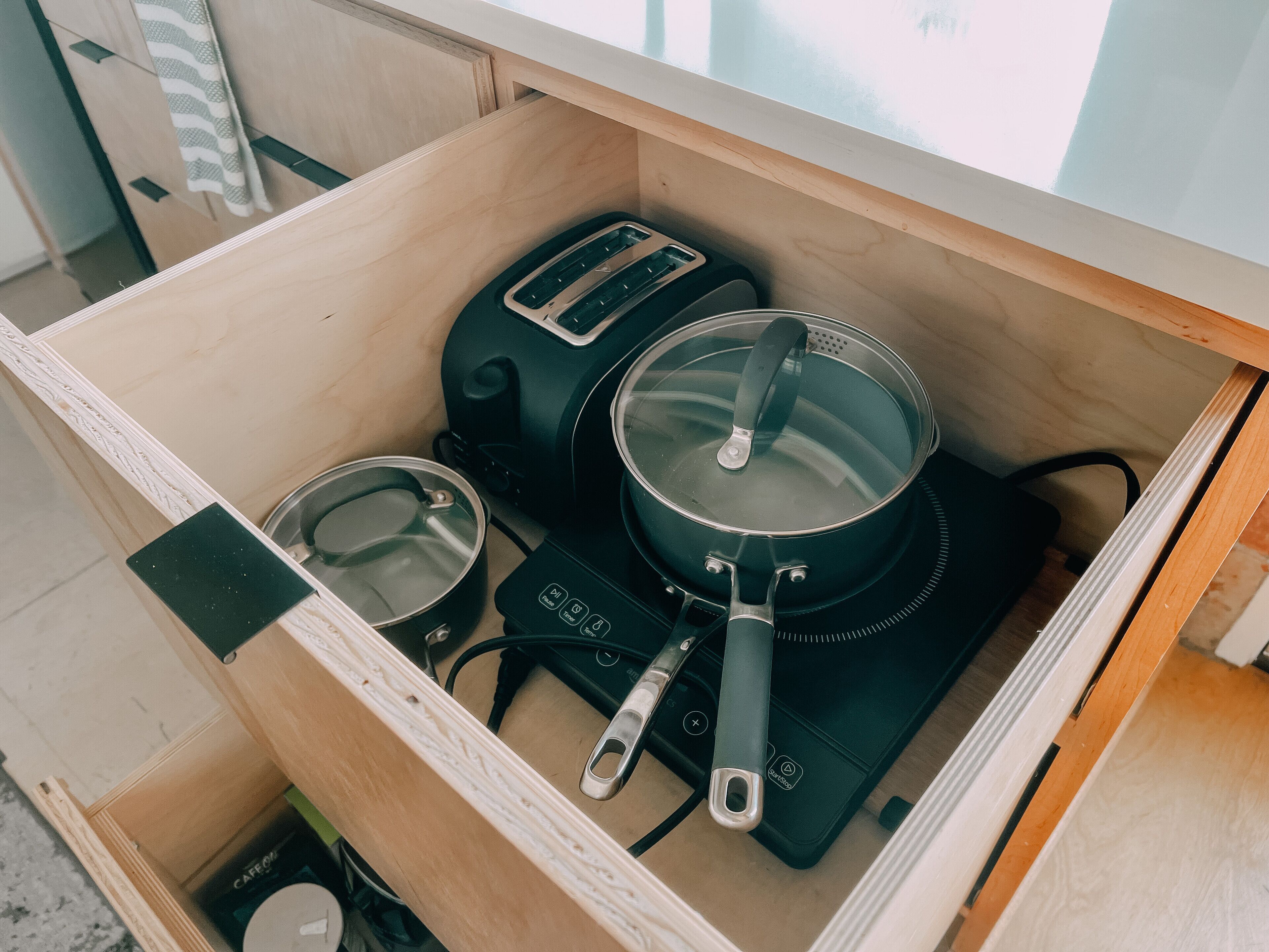 A kitchen drawer containing a toaster, a kettle, and a pot on a portable electric stove.