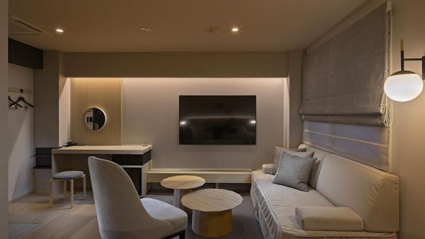 A modern, well-lit room with a sofa, two armchairs, a small coffee table, a desk, and a TV. - Hotel Palace Nagoya (Nagoya)