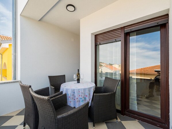 Un balcón con mobiliario de mimbre, una mesa con mantel floreado y una botella de vino.