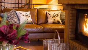 A cozy living room with a fireplace, a sofa with decorative pillows, a coffee table with books and a candle, and a staircase with wooden railings. - # Rustic, spacious, Ski-In-Ski-Out, Four Bedroom Chalet Apartment in Les Arc1950 (Bourg-Saint-Maurice)