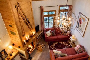 A cozy living room with a fireplace, a red sofa, a chandelier, and a window with curtains.