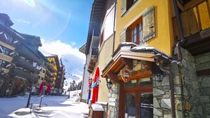 A snow-covered street with a hotel entrance, stone walls, wooden balconies, and a clear sky. - # Rustic, spacious, Ski-In-Ski-Out, Four Bedroom Chalet Apartment in Les Arc1950 (Bourg-Saint-Maurice)