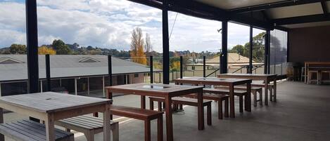 An outdoor patio with tables and benches, large windows offering a view of buildings and trees.